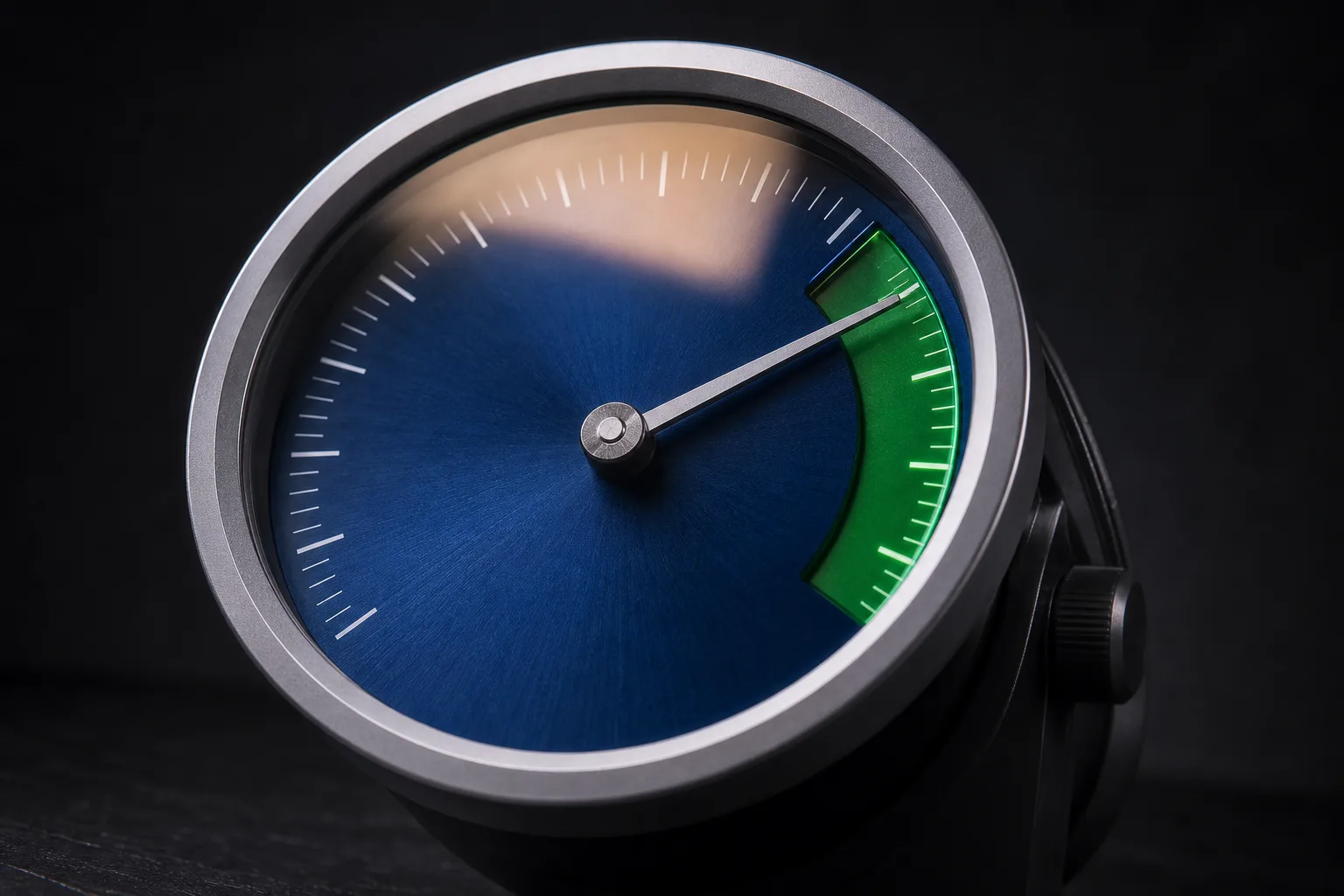 A steel gauge with a deep blue dial, its needle rising into an emerald zone
